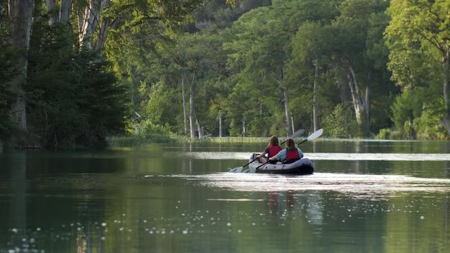 Two Women Paddle a Kayak in a Beautiful River. Long Lens. 4K UHD