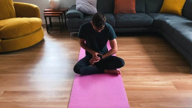 Young male practicing yoga at home, starting smartwatch to measure workout