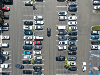 Aerial top view of parking lot at shopping mall with varieties of colored vehicles. People walking to their car and trying to park.