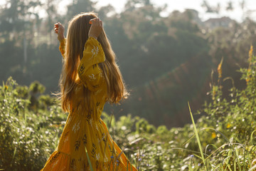 A girl in a yellow dress with long dark hair enjoys life, whirling and dancing on naure background