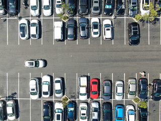 Aerial top view of parking lot at shopping mall with varieties of colored vehicles. People walking...