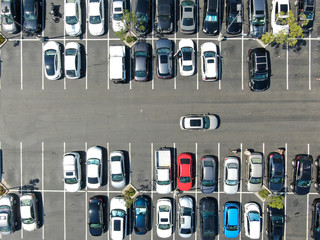Aerial top view of parking lot at shopping mall with varieties of colored vehicles. People walking...