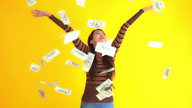 Happy asian female lottery winner throwing money, dollar cash bills, in the air. Full frame slow motion, static isolated on yellow background