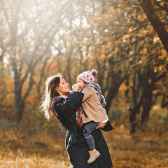 Young woman carrying her little daughter during walk in autumn park
