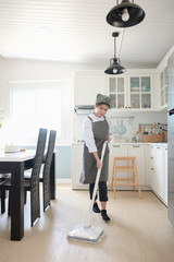A young maid cleaning the house with a mop There is a kitchen backdrop