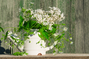 White metal teapot vase with a bouquet of white lilac flowers and grass woodlouse with green leaves.Background with a copy of the space made of old wooden boards vintage