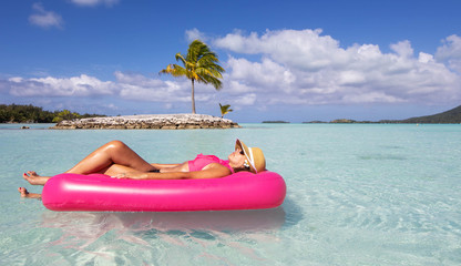 Young woman floats in paradise on a pink inflatable raft near a small tropical island on turquoise water in the South Pacific 