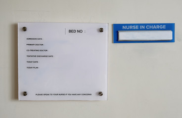 A glass information plate fixed on a hospital room wall where patient's information is written on with a name holder of the nurse on duty by the side.