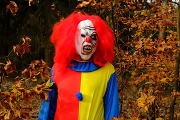 Halloween holiday.  Scary aggressive clown with red hair in the autumn forest. Creepy clown...
