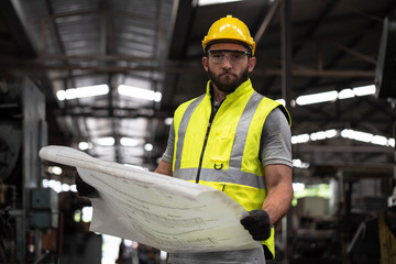 Male industrial Engineer with hardhat or helmet and vest jacket look at the information project Blueprint for working management in  industry manufacturing Factory.