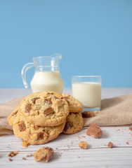 Delicious homemade chocolate chip cookies, paired with fresh milk in a glass and pitcher, placed on a white wooden floor and a blue background cloth. Drink in the morning for health and strong bones.