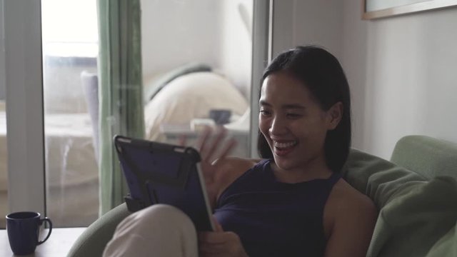 Carefree young Asian woman chats to friends on tablet, close up