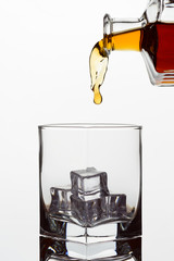Clear glass glass with ice cubes. Frozen stream from a bottle of whiskey or cognac or brandy on a white isolated background