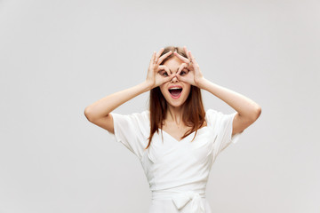 Woman holds her hands near her face in the form of a mask smile white dress 