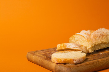 Sliced bread baguette on a wooden cutting board on a terracote color background. Close-up high quality photo.
