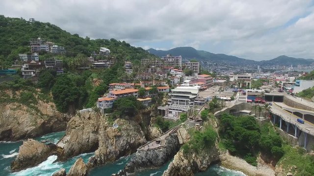Vista a&eacute;rea del famosos acantilados en la zona de La Quebrada en  Acapulco, Guerrero. El drone volando hacia arriba con un cielo azul como fondo.