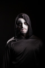 Man with scary make up for halloween wearing a hood isolated over black background.