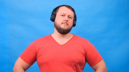 Fototapeta premium Cheerful charismatic fat man in headphones isolated and pink t-shirt on a blue background. listen to music, sing and dance