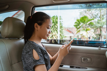 Teenage girl using a smartphone and look to screen while sitting in the car with the window open while traveling