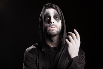 Spooky man dressed up like a grim reaper over black background. Halloween mystery.