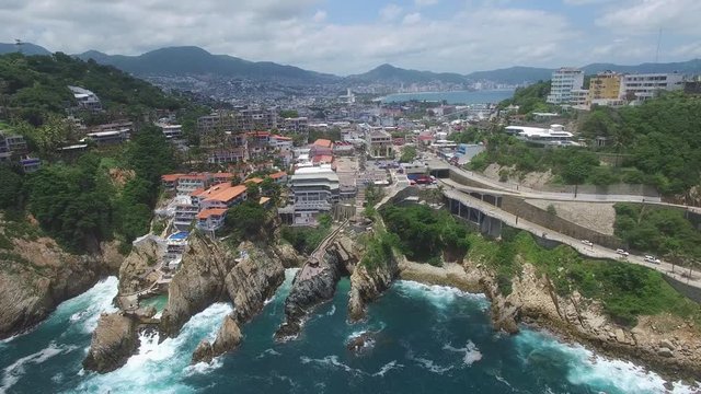 Vista a&eacute;rea frente al famoso acantilado de La Quebrada con la Bah&iacute;a de Acapulco y un cielo azul como fondo
