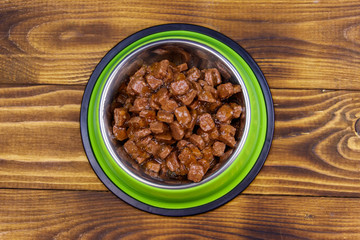 Canned food for cats or dogs in green metal bowl on wooden floor. Top view