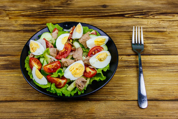 Tasty tuna salad with eggs, lettuce and fresh vegetables on wooden table