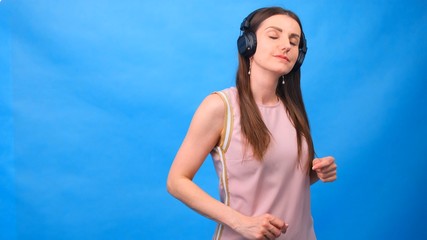 Beautiful Energy Girl with headphones listening to music on a blue background in the studio