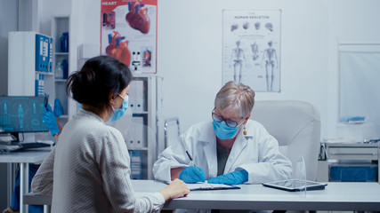 Physician consultation during COVID 19 health crisis, doctor and patient wearing masks, talking through a plexiglass wall. Medical consultation in protective equipment concept shot of sars-cov-2