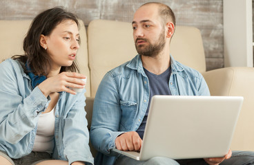 Couple relaxing in living room drinking coffee and browsing on internet.