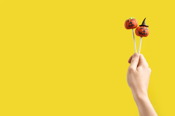 Woman with delicious pumpkin shaped cake pops and space for text on yellow background, closeup. Halloween celebration