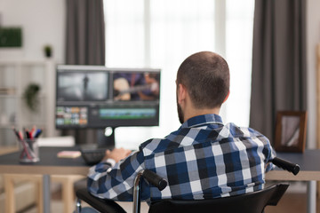 Handicapped film maker in wheelchair working film post production. Invalid videographer doing his business online, using high technology, sitting in his apartment, working remotely in special