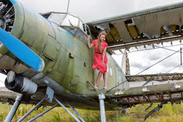 Pretty young adult woman stands on the wing of an abandoned green plane