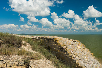 An Old Citadel Wall Facing the Green Lake and a Beautiful Sky Background with White Clouds (Dobrogea, Romania)