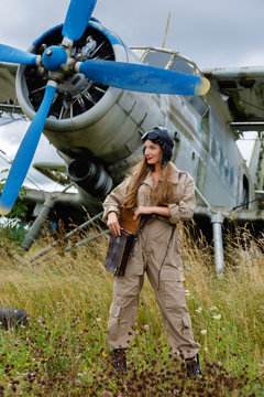 Pretty woman in a helmet and pilot's suit standing next to the plane