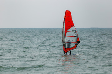 A red sailboat surfing and sailing on the sea near the beach in Pattaya beach of eastern in Thailand on a long holiday.