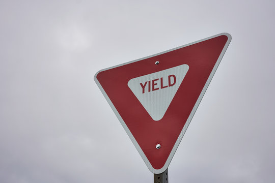 Yield sign against overcast sky background. A give way sign which indicates that merging drivers must prepare to stop if necessary to let a driver on another approach proceed.
