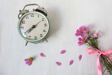 Clock with a bouquet of delicate summer flowers and scattered petals on a white background, top...