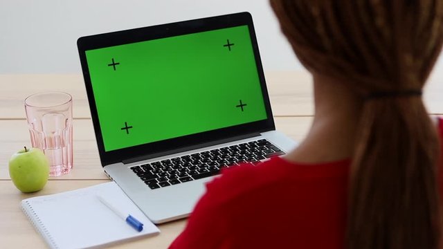 woman studying using laptop with green screen Spbi. afro female listen watch something on computer with notebook and pen on desk. concept mock up, chroma key. copy space screen for student