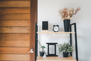 Wooden shelf with bouquet of dry flower,grass in pot, greenery in vase, alarm,photo frame and black board  over white wall  decoration in living room at home
