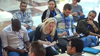 diverse multicultural group of attentive people listen to conference seminar coaching irrl write notes in notebook. top view of listeners with badge, lecture about business