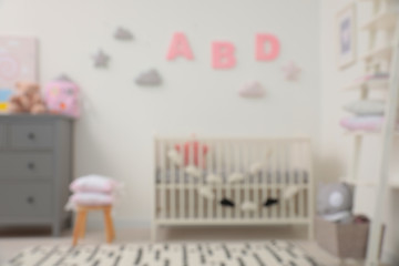Blurred view of cute baby room interior with modern crib near white wall