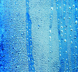 Drops of water on blue glass as an abstract background