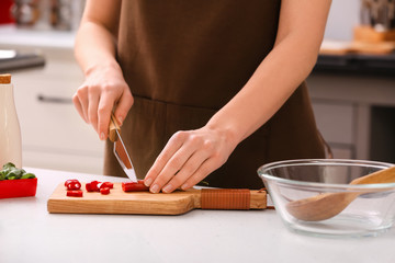 Woman cutting hot chili pepper in kitchen