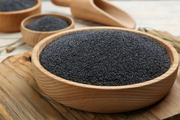 Poppy seeds in bowl on wooden board, closeup