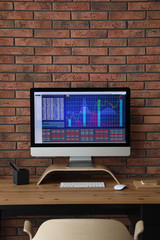 Fototapeta premium Modern computer with statistic information on wooden table near brick wall