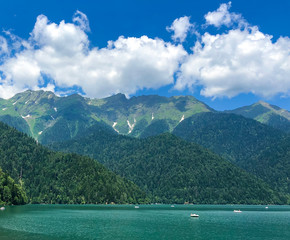 Mountain glacial lake Ritsa in Abkhazia. Located at an altitude of 950 meters above sea level, among high green mountains. Blue sky with white fluffy clouds.