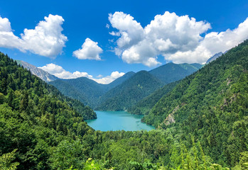 Blue lake of Abkhazia, high in the mountains, among greenery. Blue sky with white clouds.