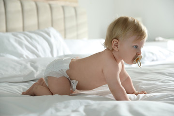 Cute little baby in diaper with pacifier lying on bed at home