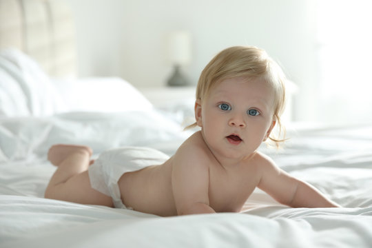 Cute little baby in diaper lying on bed at home
